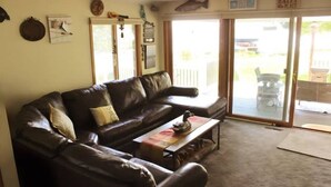 A living room with a brown leather couch, a coffee table, and a glass door leading to an outdoor area. - Entire 3 Bedroom Lake House in Beaver Dam (Beaver Dam)