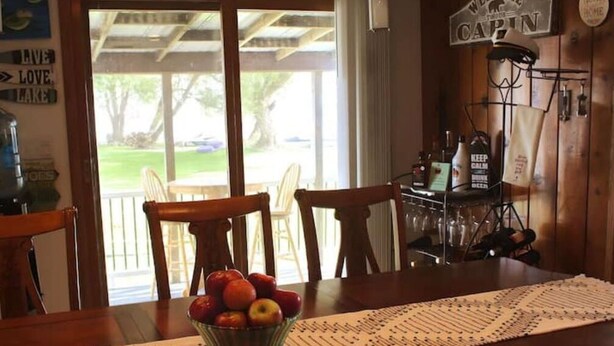 A dining area with a table set for four, a bowl of fruit, and a view of the outdoors. - Entire 3 Bedroom Lake House in Beaver Dam (Beaver Dam)
