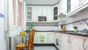 Una cocina con armarios blancos, una mesa de vidrio y un lavabo.