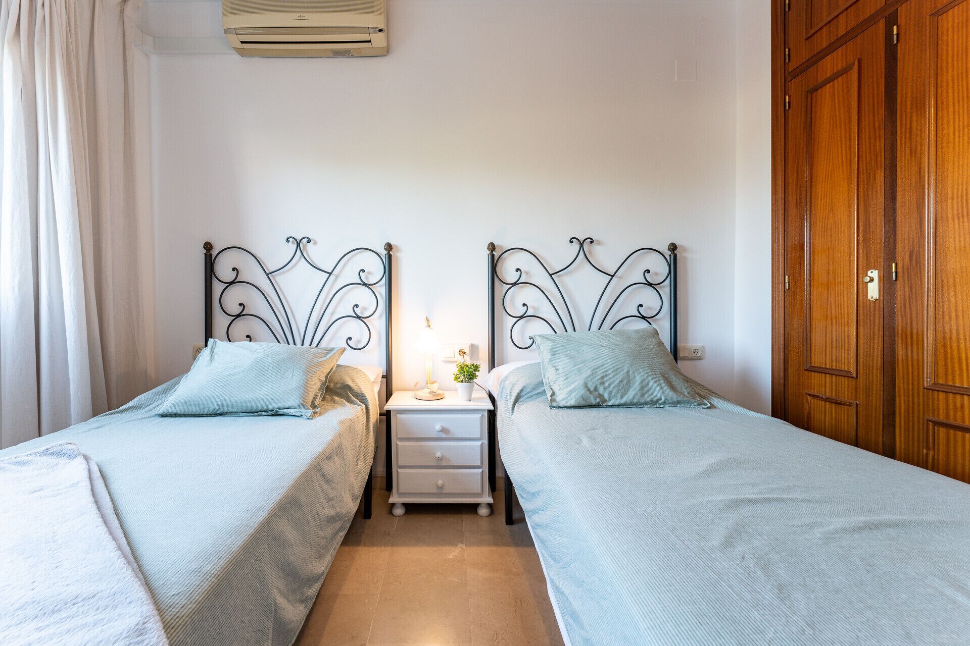 A room with two beds, a nightstand, a lamp, and a wooden wardrobe.