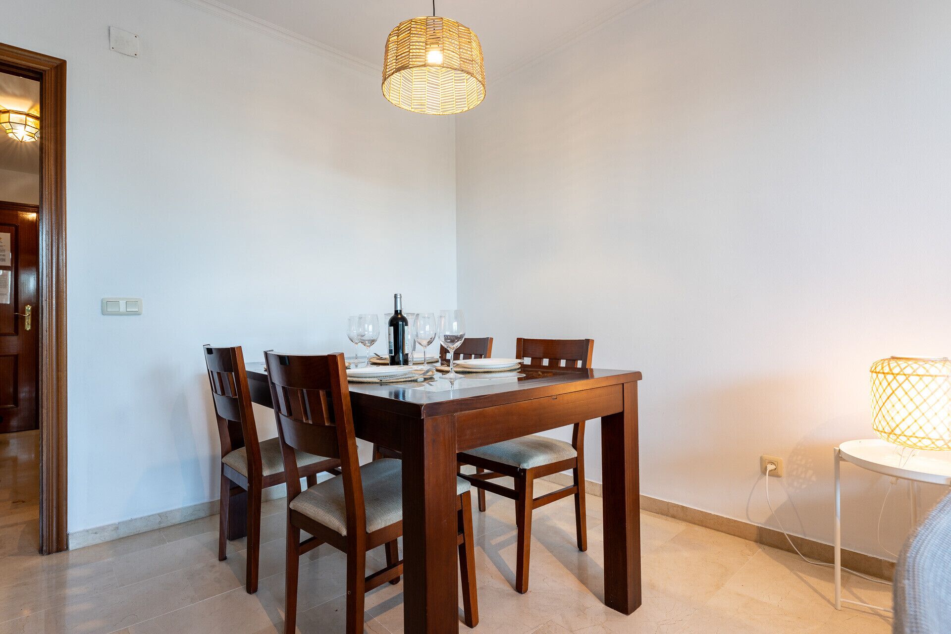 A dining area with a wooden table, four chairs, and a hanging light fixture.