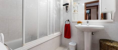 A bathroom with a white toilet, a sink, a mirror, and a shower with frosted glass doors.