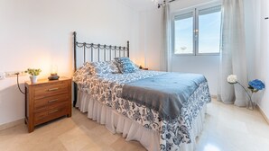 Un dormitorio con una cama, una mesita de noche de madera y un ventanal con cortinas.