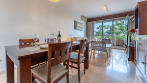Un comedor con una mesa y sillas de madera, una lámpara colgante y vistas al exterior a través de amplios ventanales.