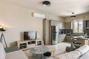 A modern kitchen with stainless steel appliances, a dining area with a round table, and a living room with a sofa and a TV.