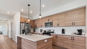 Una cocina moderna con armarios de madera, electrodomésticos de acero inoxidable e iluminación colgante.