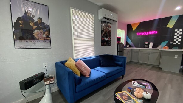 Una sala moderna con un sofá azul, una mesa de centro de vidrio y una cocina al fondo.