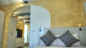 Un dormitorio con pared de piedra, una cama con dos almohadas, un aparador y un espejo.