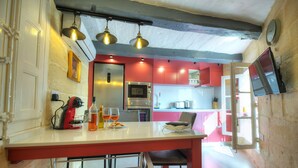 Una cocina moderna con armarios rojo y blanco, un refrigerador de acero inoxidable y un horno empotrado. Hay lámparas colgantes sobre la encimera y un televisor de pantalla plana montado en la pared.