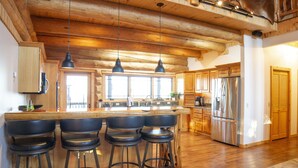 Una cocina amplia con vigas de madera, una isla grande con taburetes de bar, electrodomésticos de acero inoxidable y una puerta de madera.