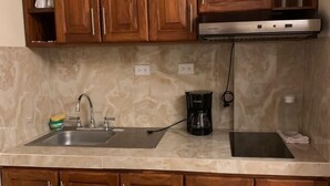 A kitchen with wooden cabinets, a stainless steel sink, a coffee maker, and a stove. - Luna de Plata (Quetzaltenango)