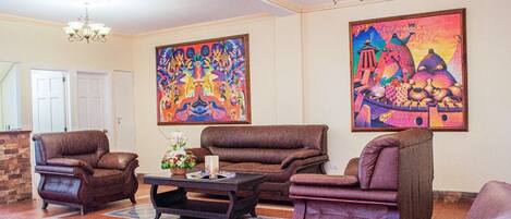 A living room with brown leather sofas, a coffee table, and two paintings on the wall.