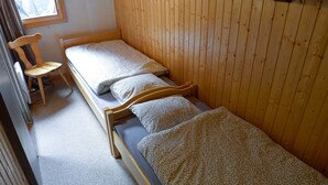Una habitación pequeña y funcional con dos camas individuales y una silla de madera.