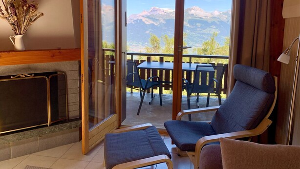 Una habitación acogedora con chimenea, una mesa de comedor con sillas y vistas a montañas a través de amplios ventanales.