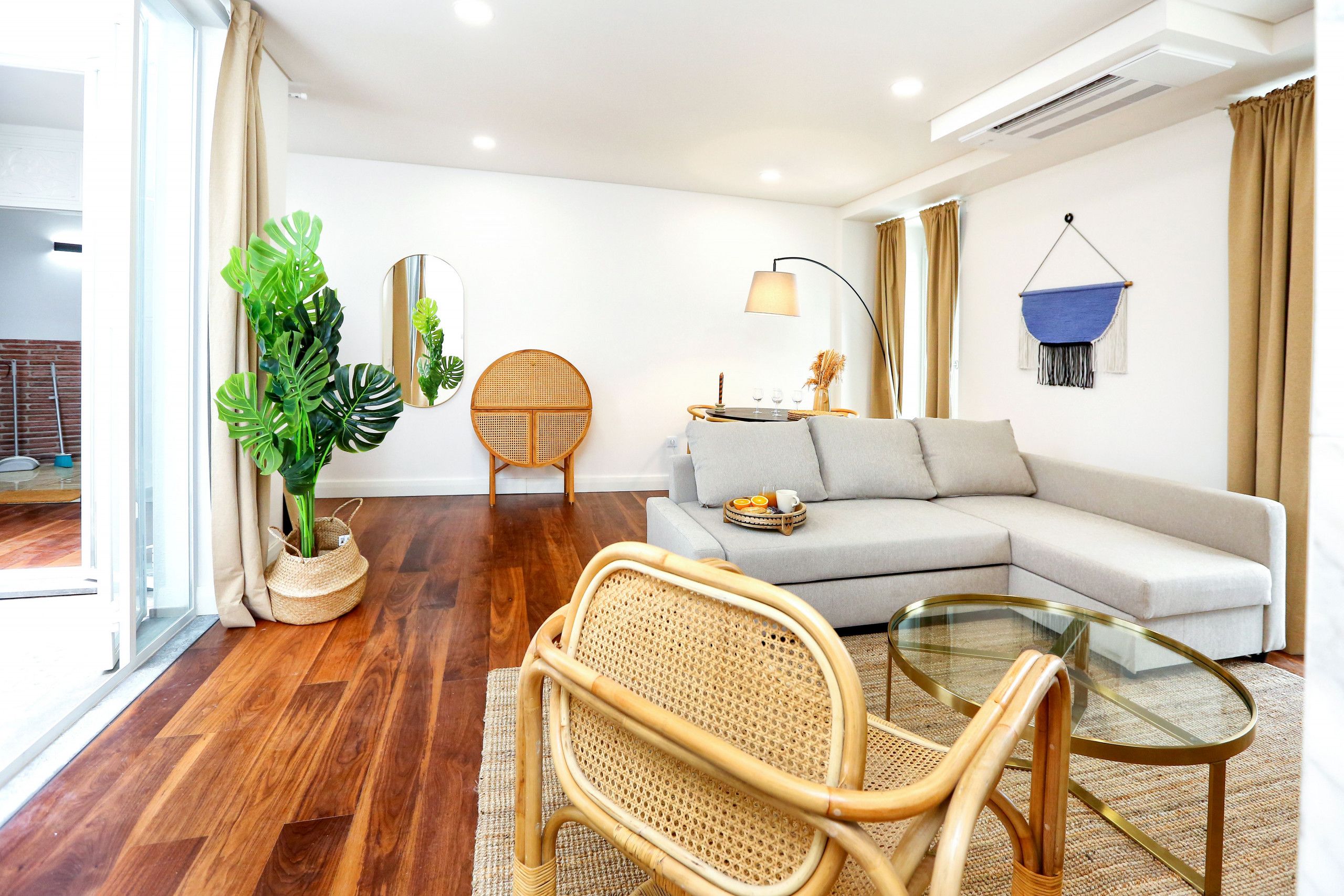 A modern living room with a sofa, a glass coffee table, a rattan chair, a potted plant, and a hanging blue textile.