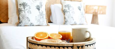 A breakfast tray with orange slices, a glass of orange juice, and a cup on a bed with white bedding and patterned pillows.