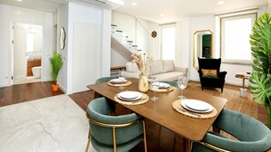 A dining area with a wooden table set for four, green upholstered chairs, and a staircase leading to an upper level. - GREEN FARO : MODERN DUPLEX WITH A BLISS TERRACE (Faro)