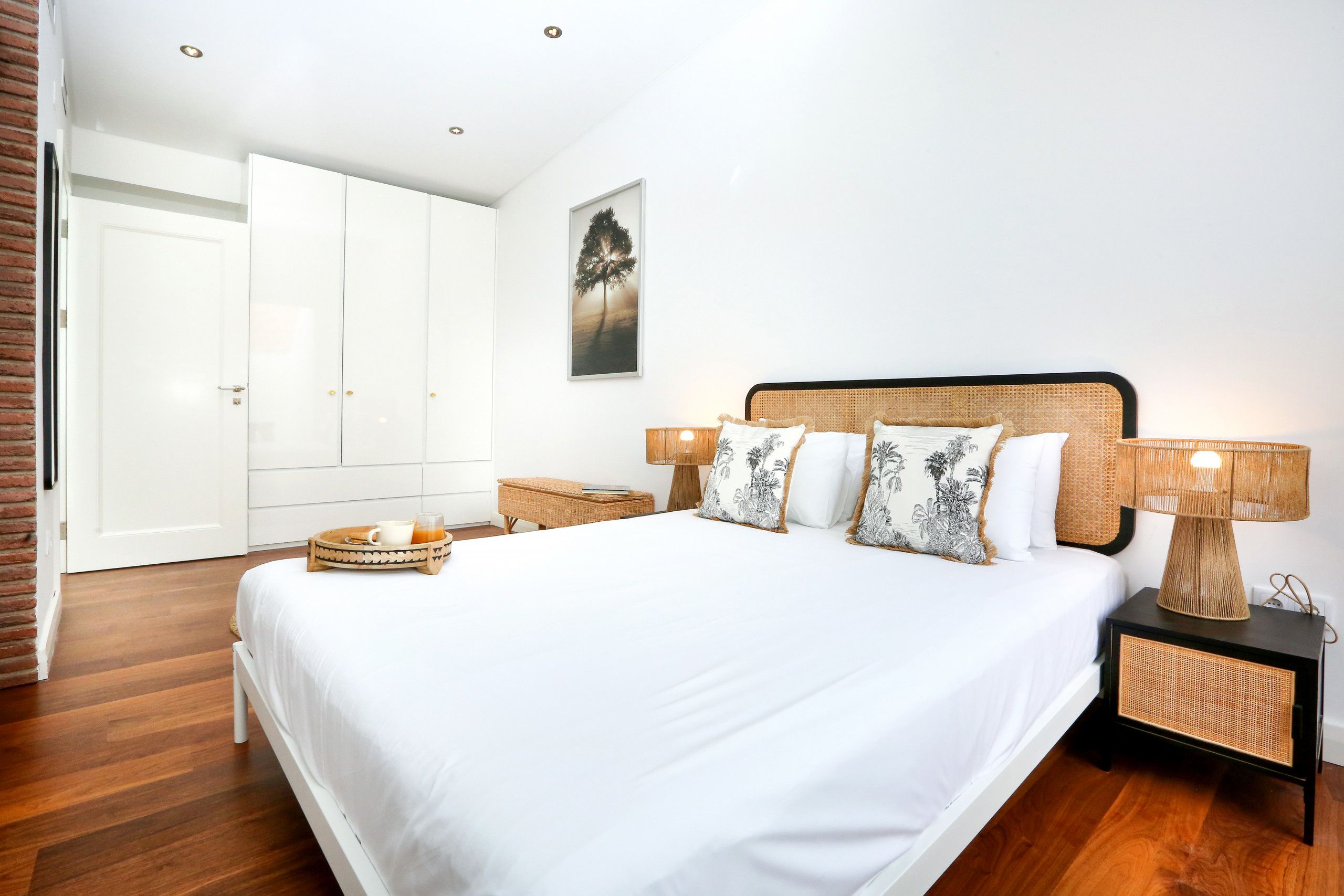 A neatly arranged bedroom with a large bed, bedside tables, a wicker lamp, and a framed picture on the wall.