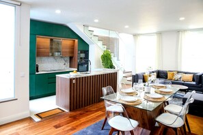 A modern kitchen with green cabinets, a dining area with a glass table, and a staircase leading to a living room.