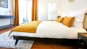 Un dormitorio con cama, escritorio, silla, espejo y puerta.