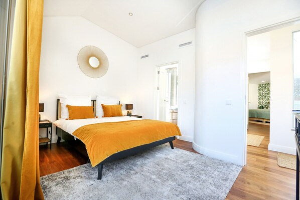 A bedroom with a bed, bedside tables, a round wall decoration, and a doorway leading to another room.