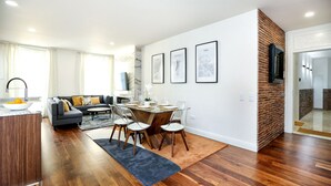 Una sala de estar moderna con comedor, pisos de madera, un sofá, una mesa de centro y una encimera de cocina con fruta.