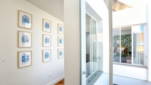 Un pasillo con obras de arte enmarcadas en la pared, una puerta de cristal que da a un balcón y suelo de madera.