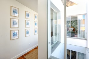 Un couloir orné de tableaux encadrés, une porte vitrée donnant sur un balcon et un plancher en bois.
