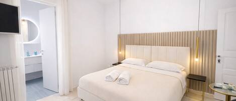 A hotel room with a large bed, a bedside table, a TV mounted on the wall, and a bathroom visible through an open door.