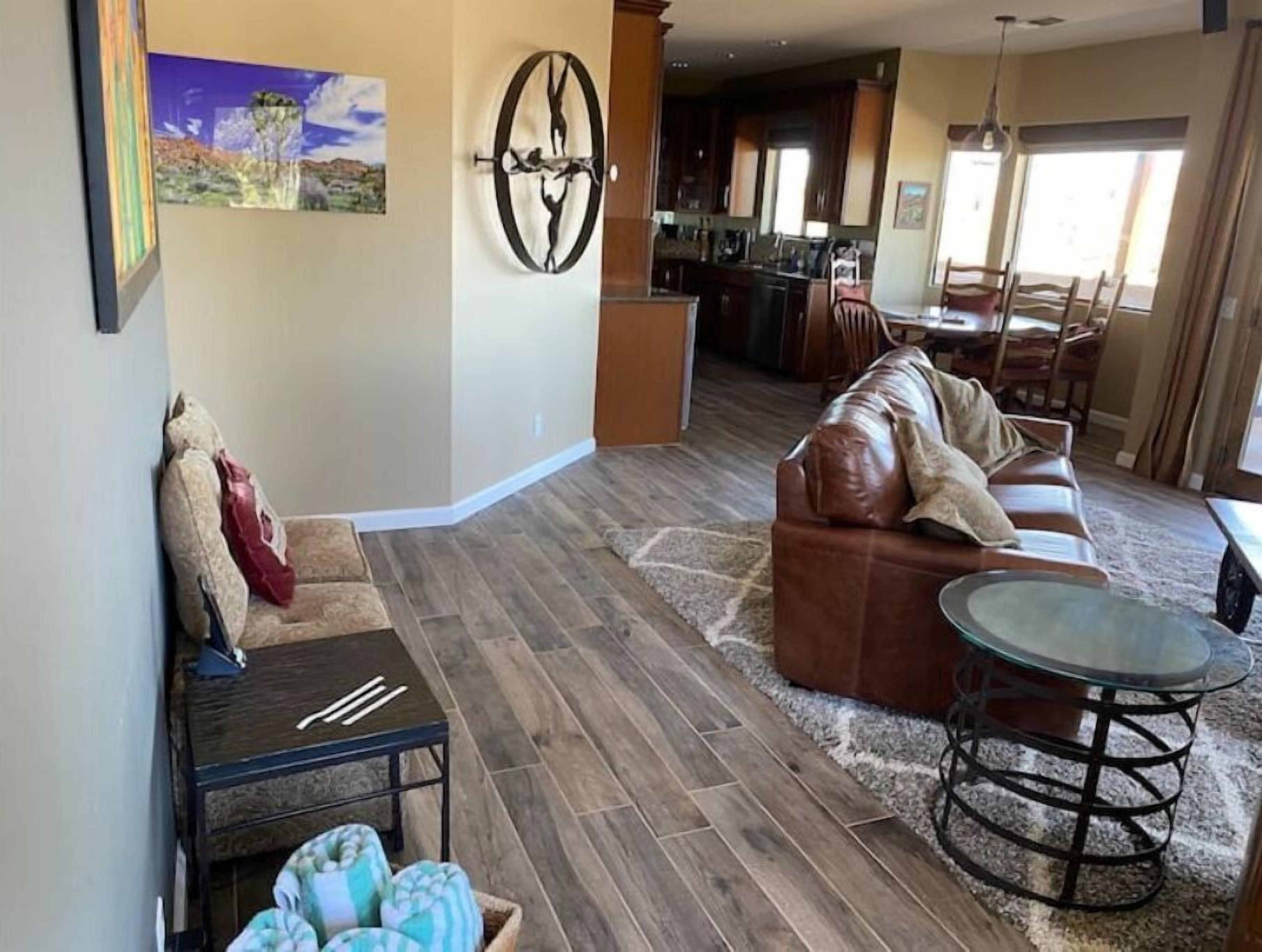 A living room with a brown leather sofa, a glass coffee table, and a dining area with a kitchen in the background.