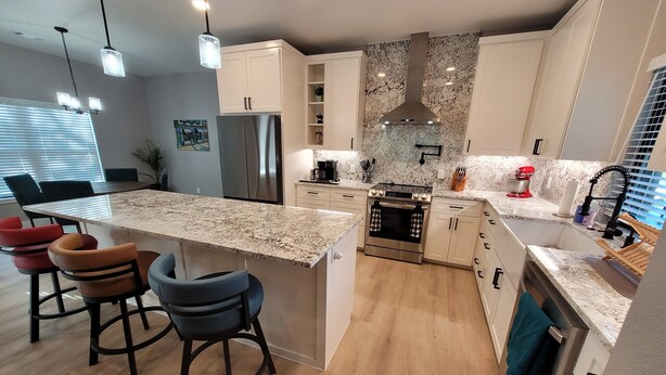 A modern kitchen with a central island, bar stools, a stainless steel refrigerator, a stove, and a sink.