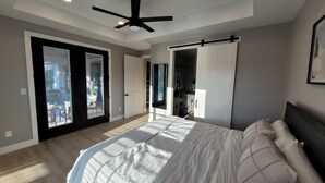 A bedroom with a large bed, a ceiling fan, and a sliding door leading to a balcony.