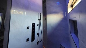 A modern bathroom with a shower, a control panel, and a ceiling light fixture.
