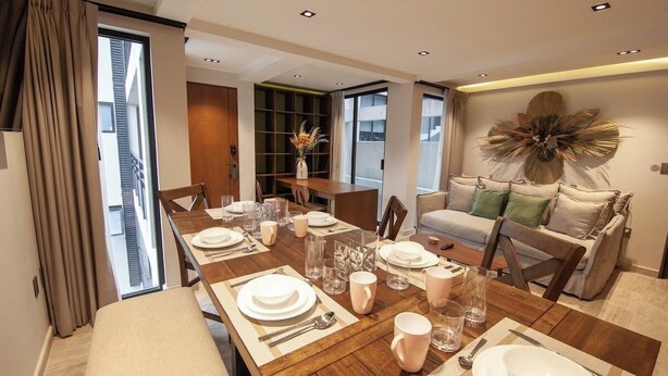 A modern dining area with a wooden table set for four, a sofa, and a bookshelf.