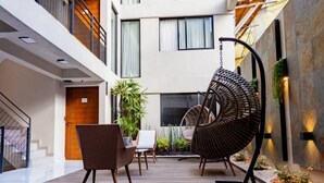 A modern indoor courtyard with wicker furniture, a hanging chair, and a staircase.