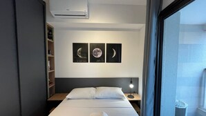 Une chambre d’hôtel comprenant un lit, une table de chevet, un climatiseur fixé au mur et trois tableaux représentant la lune.