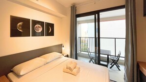 Une chambre d’hôtel comprenant un lit, une table de chevet, un climatiseur fixé au mur et un balcon avec une table et des chaises.