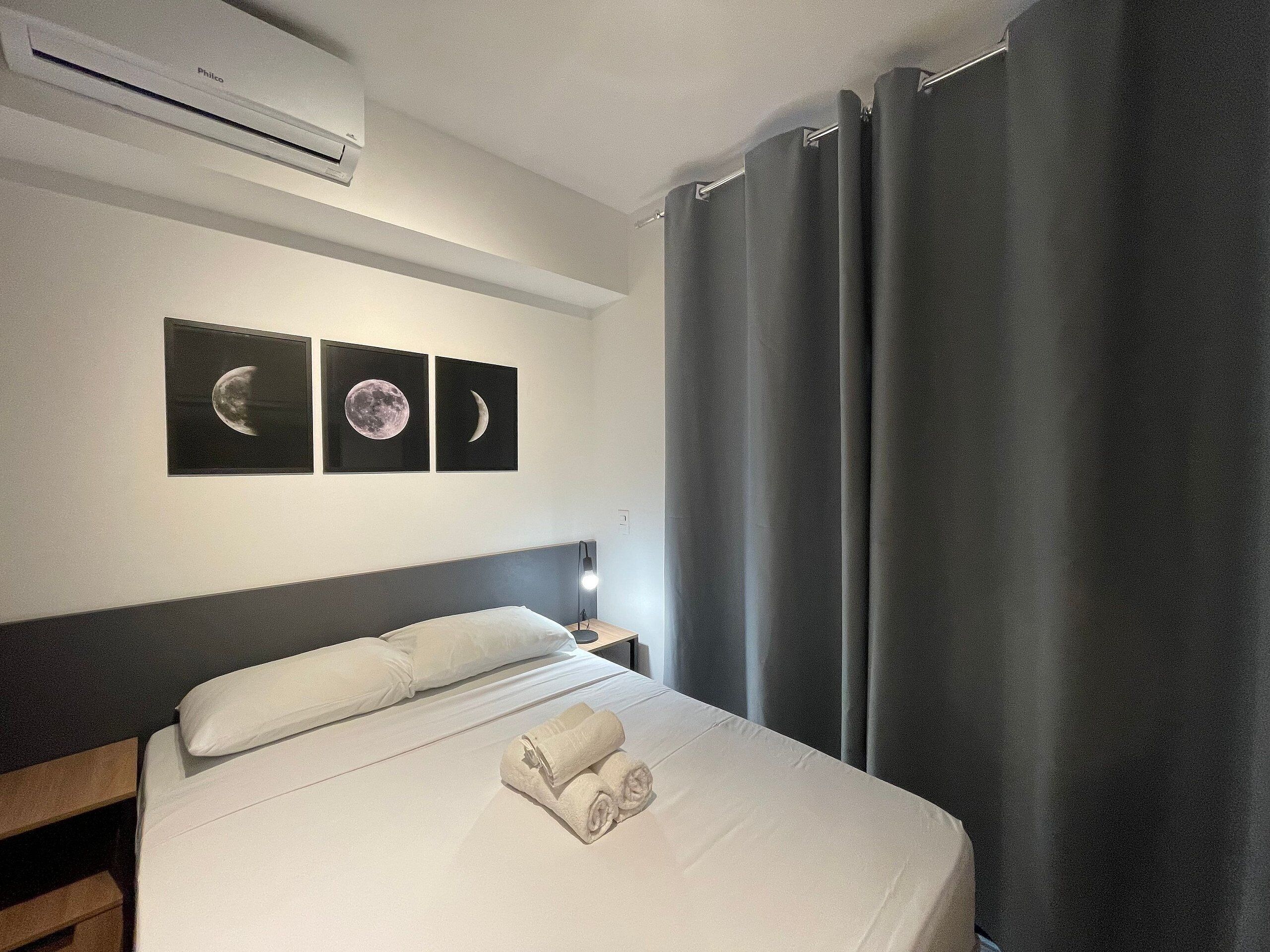 Hotelkamer met een bed, nachtkastje, een wandairconditioner en twee inlijstingen met afbeeldingen van de maan.