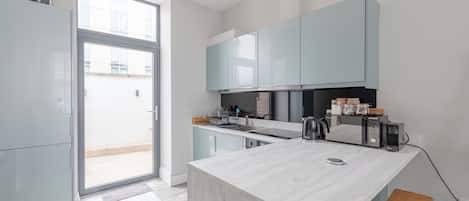 Une cuisine moderne dotée d’un grand îlot central, de meubles de couleur bleu clair et d’une porte-fenêtre coulissante donnant sur un balcon.