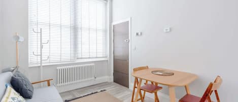 Une pièce comprenant un lit, une table avec des chaises, un radiateur et une fenêtre avec des stores.