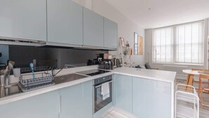 A modern kitchen with a central island, built-in appliances, and a dining area with a table and chairs. - Chic 1BD Flat with Patio, 2 Mins from Barons Court (London)