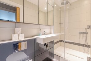 Een moderne badkamer met een glazen douchecabine, een wit wastafelmeubel en een toilet.