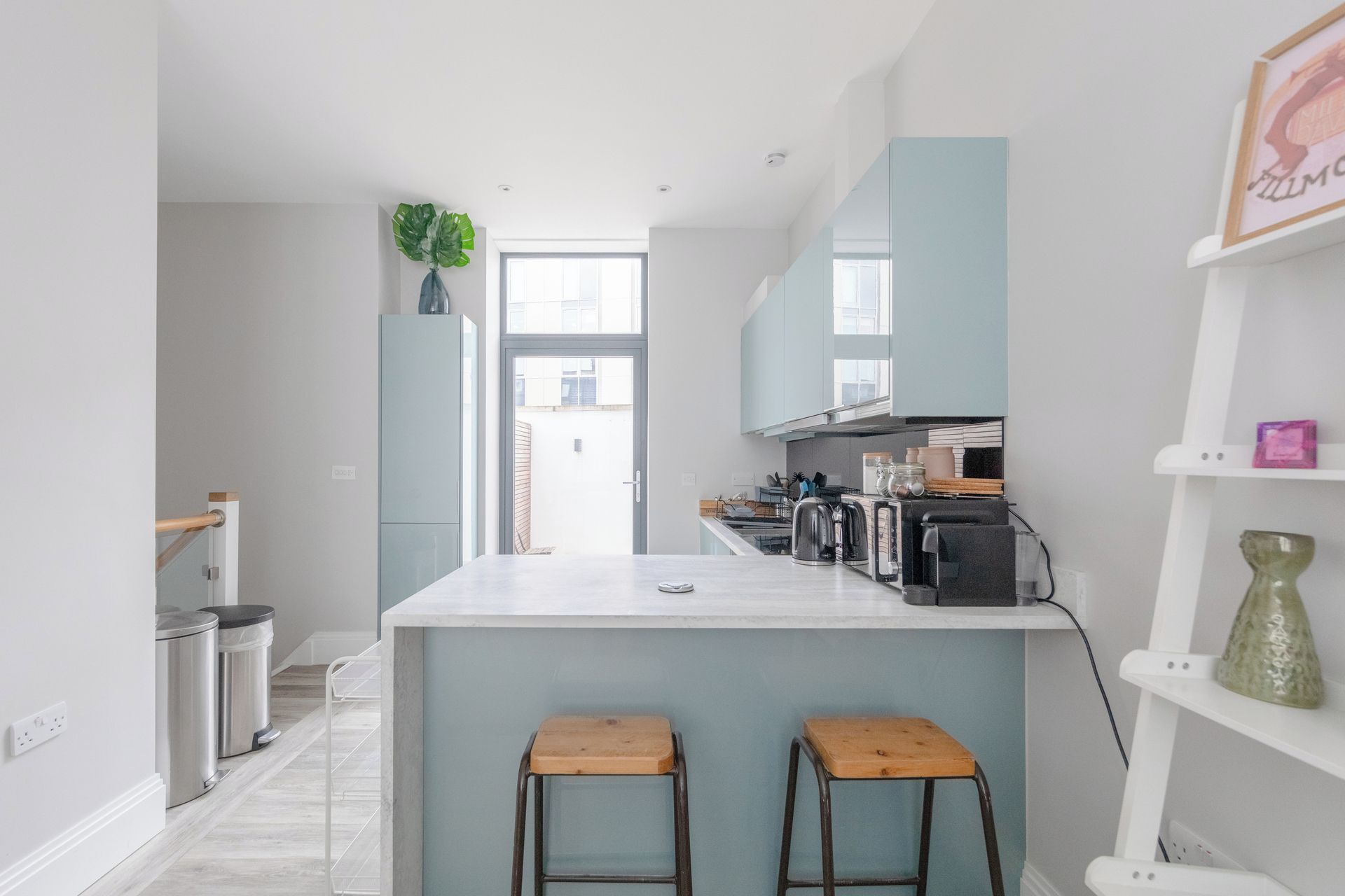 A modern kitchen with a central island, bar stools, and a view to the outside.