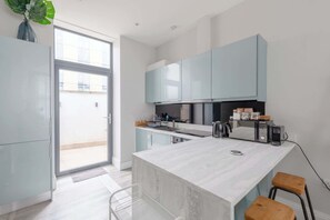 Une cuisine moderne dotée d’un îlot central, de meubles de couleur bleu clair et d’une porte-fenêtre coulissante donnant sur un espace extérieur.