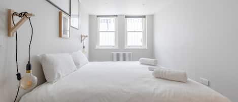 A minimalist bedroom with a large bed, two windows, and a radiator.