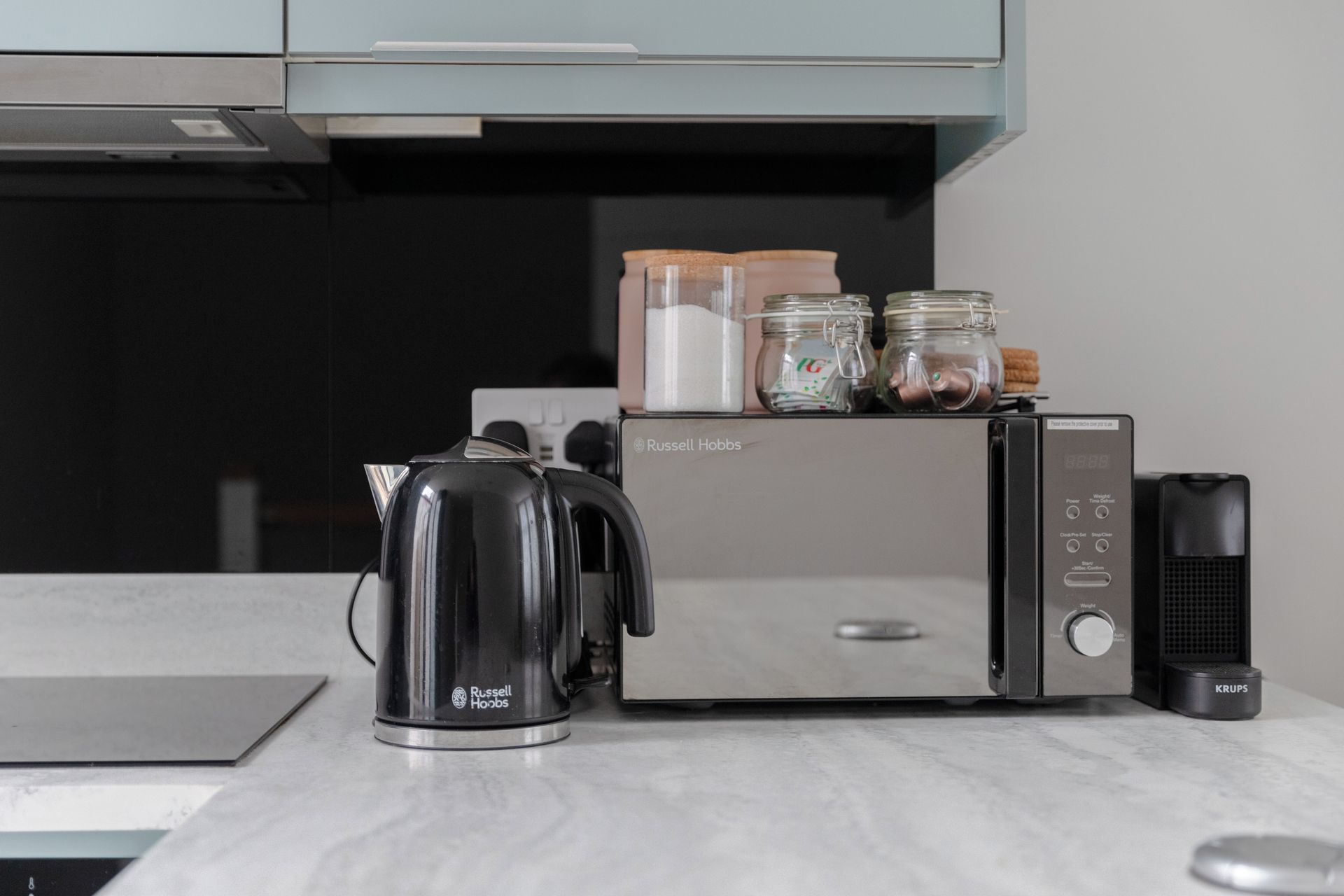 Eine moderne Küche mit einem Edelstahl-Wasserkocher, einer Mikrowelle und einer Krups-Kaffeemaschine auf der Arbeitsfläche.