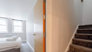 A hotel room with a bed, a window, a radiator, and a staircase. - Chic 1BD Flat with Patio, 2 Mins from Barons Court (London)