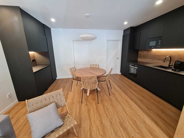 Una cocina moderna con armarios oscuros, una mesa redonda de madera y un horno empotrado.