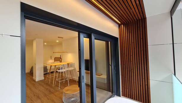 Un intérieur moderne avec un coin repas comprenant une table en bois et des chaises blanches, une porte vitrée donnant sur une autre pièce et un mur en bois à lattes.