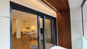 Un interior moderno con comedor que presenta una mesa de madera y sillas blancas, una puerta de vidrio que da a otra habitación y un muro de listones de madera.